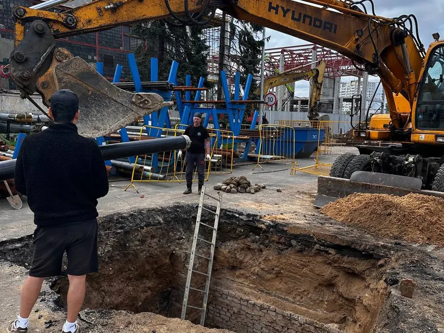 Экскаватор разрабатывает приёмный котлован на городском объекте